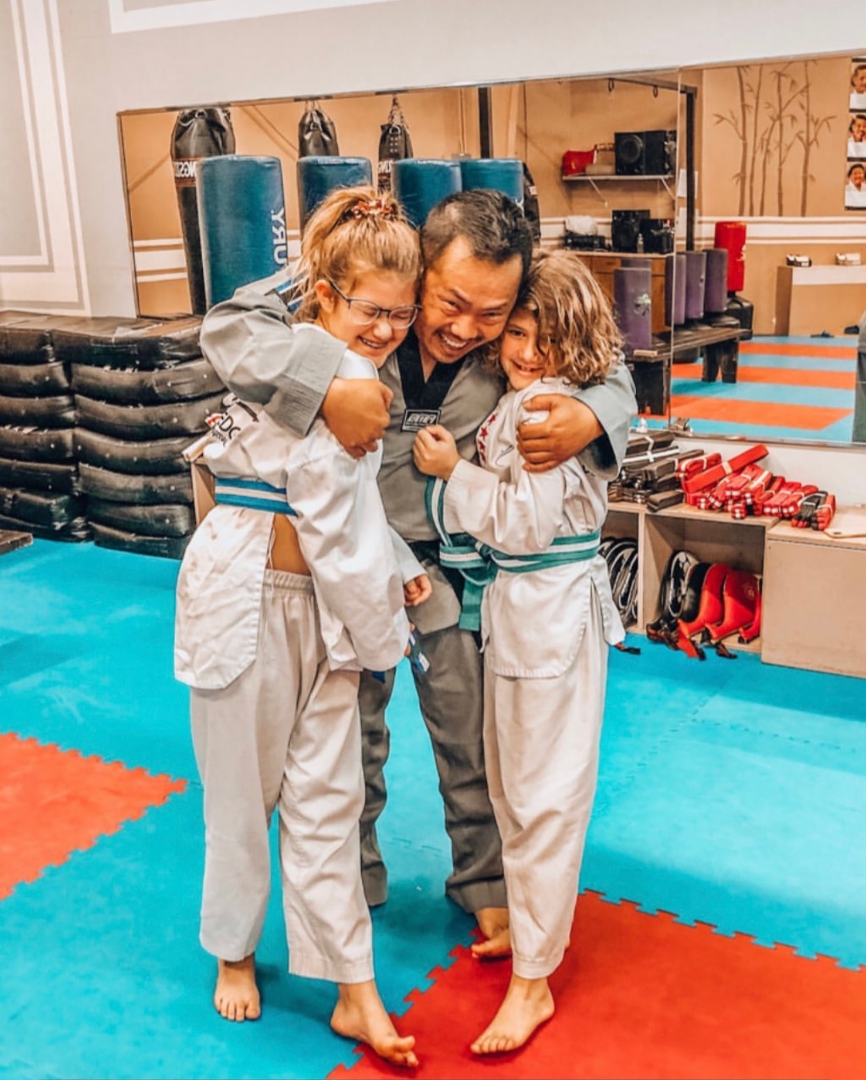 Martial arts instructor embracing two young students in the studio