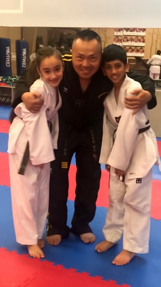 Martial arts instructor posing with two young students on training mats